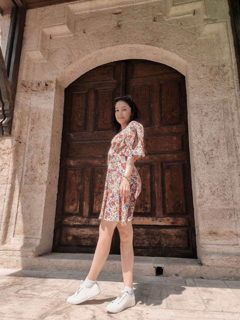 Girl in front of a big gate. Historical setting. Sunny.